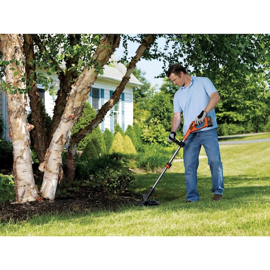Photo of person using BLACKDECKER GLC3630L20 grass trimmer on lawn near trees and house.