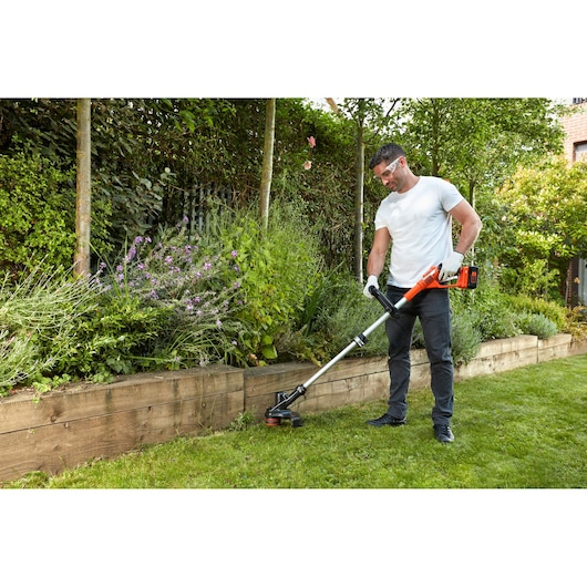 BLACKDECKER GLC3630LB cordless grass trimmer used for garden edge trimming near raised wooden planter.