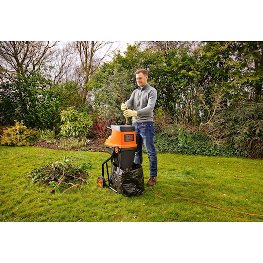 Man using BLACKDECKER GS2400 garden shredder in backyard, feeding branches into orange and black machine.