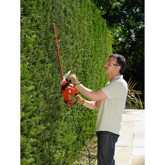 Photo of a person trimming a hedge with a BLACKDECKER GT5050 corded hedge trimmer outdoors.