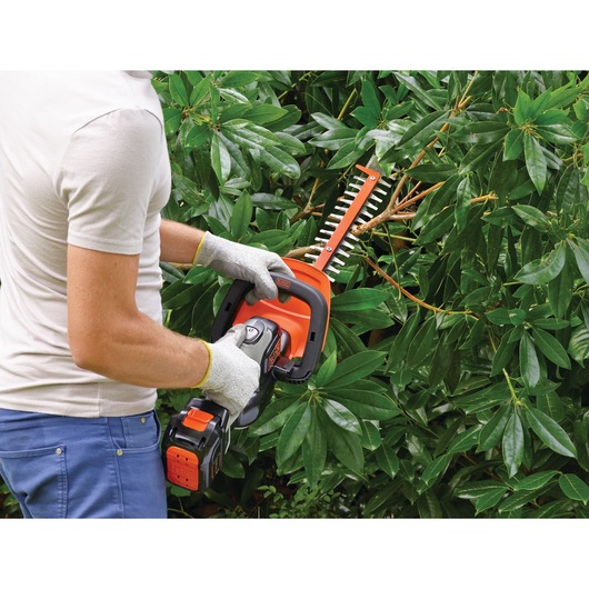 BLACKDECKER GTC5455PC hedge trimmer in use, person trimming green bushes outdoors, side view.