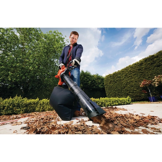 BLACKDECKER GW2810 leaf blower and vacuum used outdoors for clearing dry leaves, shown in garden.