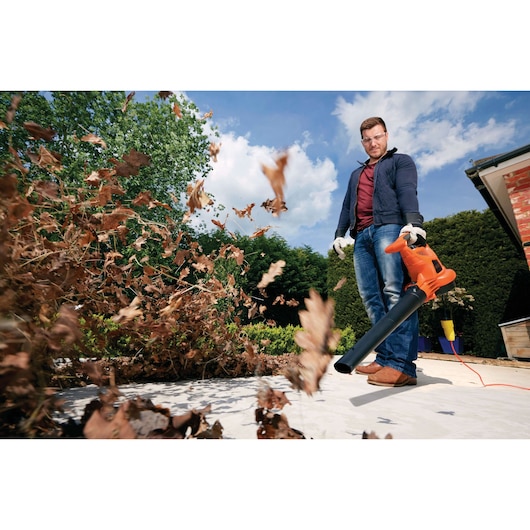 BLACKDECKER GW3030 leaf blower in use outdoors, blowing dry leaves with orange and black design.