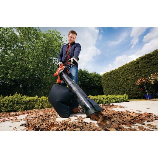 BLACKDECKER GW3030 leaf blower with collection bag in use, clearing dry leaves on a garden path.