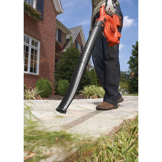 BLACKDECKER GWC1800L20 leaf blower clearing grass on a sidewalk in front of a brick house.