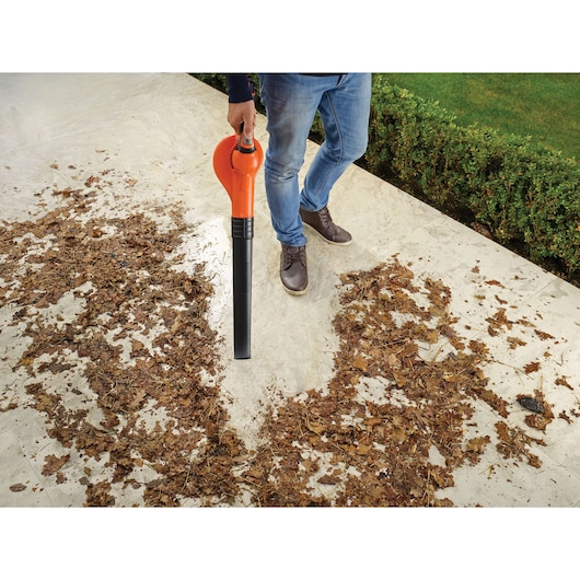Photo of BLACK+DECKER GWC1820PC cordless leaf blower in use clearing leaves on a stone patio.