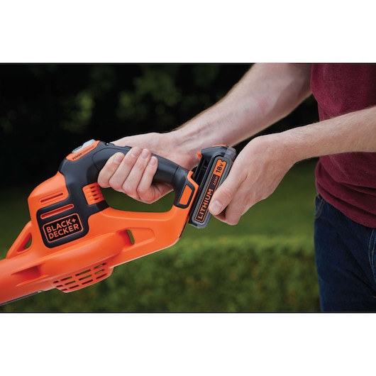 Photo of BLACK+DECKER GWC1820PC orange cordless leaf blower, close-up of hands inserting 18V lithium battery.