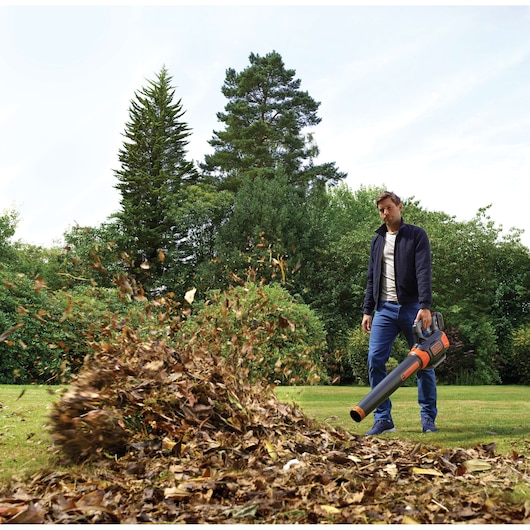 BLACKDECKER GWC54PC orange and black cordless leaf blower in use outdoors with leaves being blown on grass.