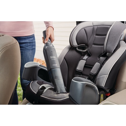 BLACKDECKER HLVC320B11 handheld vacuum cleaning crumbs from a car seat in close-up photography.