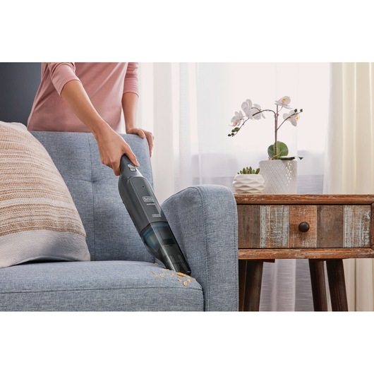 BLACK+DECKER HLVC320B11 handheld vacuum cleaning sofa crumbs in living room.