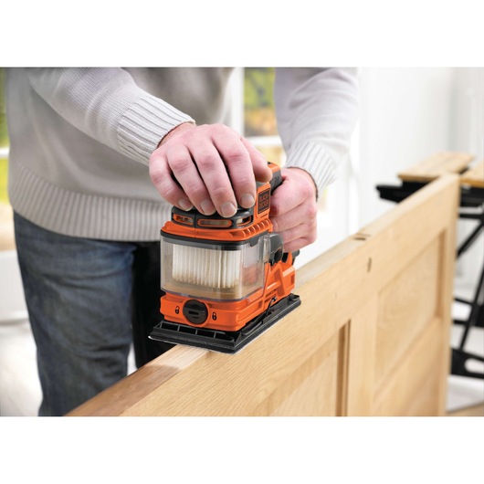 BLACKDECKER KA330EKA orange electric sander with dust collector used on wooden door, close-up view.