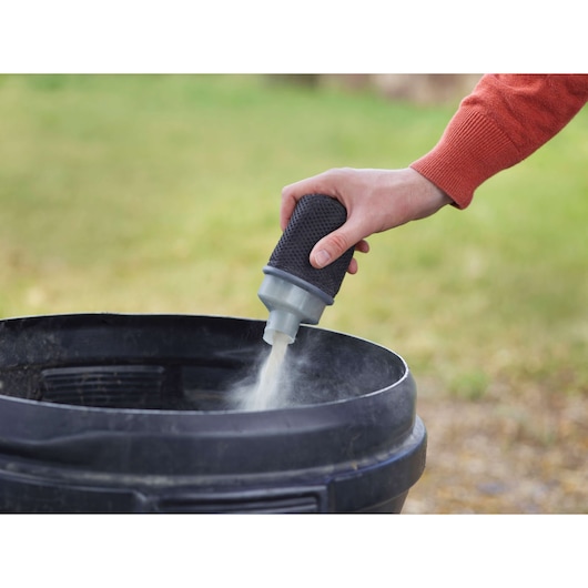 BLACKDECKER KA450 dust filter pouring debris into a black bin outdoors, close-up view.