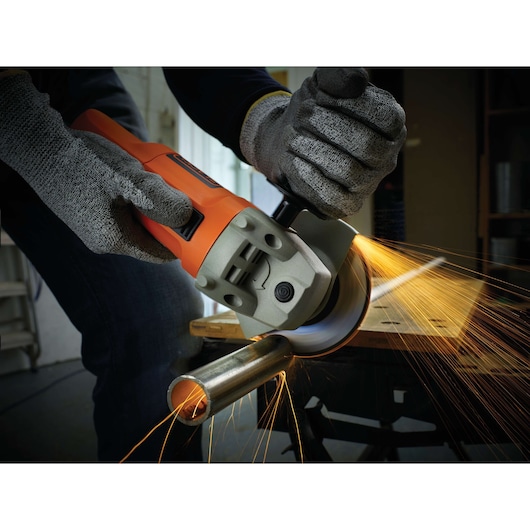 BLACKDECKER KG115 angle grinder cutting metal pipe, sparks flying, orange casing, protective gloves worn.