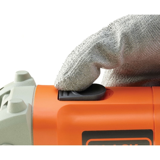 Photo of a gloved hand pressing the power switch on an orange BLACKDECKER KG115 angle grinder, side view.