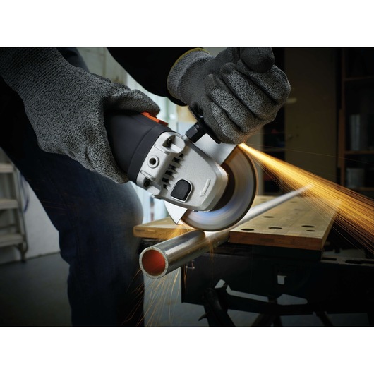 BLACKDECKER KG911K angle grinder cutting metal pipe, safety gloves worn, close-up action shot.
