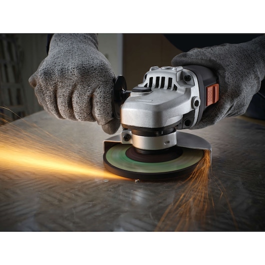 A close-up of gloved hands using a BLACK+DECKER angle grinder on a metal surface, with sparks flying from the grinding wheel.