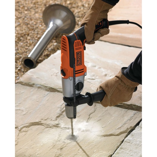 Photo of BLACK+DECKER KR1102K hammer drill in use on stone surface, close-up in outdoor setting.