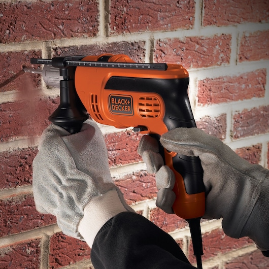 BLACK+DECKER KR604CRESK orange and black corded hammer drill used on brick wall.