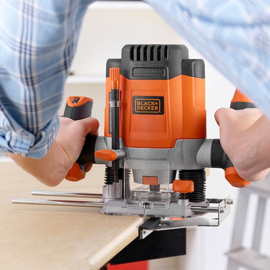 Black+Decker KW1200EKA plunge router in use on wood, close-up showing hands operating the tool.