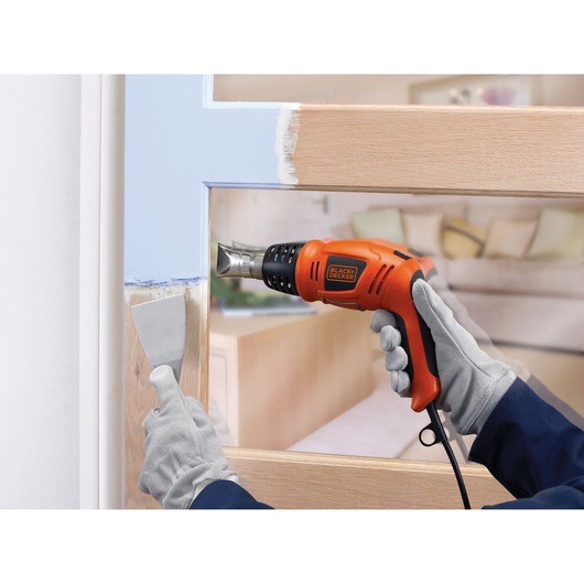 BLACKDECKER KX1693 heat gun used to remove paint from a wooden door, close-up with gloved hands.