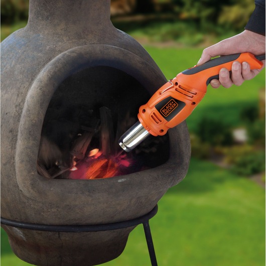 BLACKDECKER KX1693 orange heat gun igniting wood in an outdoor fireplace, handheld in use.
