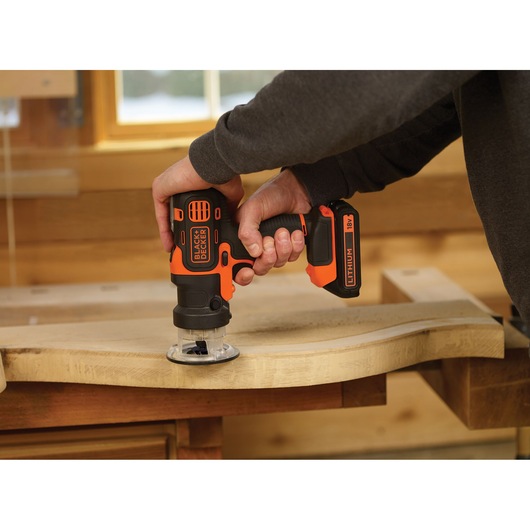 BLACK+DECKER MT218K cordless 18V multi-tool in use on a wood surface, close-up of hand holding tool.