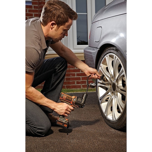 Photo of a person using a BLACKDECKER MTNF9 cordless inflator on a car tire outdoors.