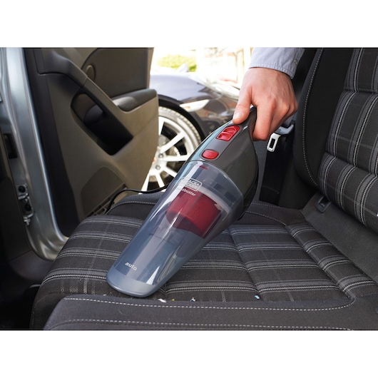 BLACKDECKER NV1210AV handheld vacuum cleaner used on car seat, compact grey and red design.