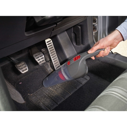 Photo of BLACKDECKER NV1210AV handheld vacuum cleaning car floor near pedals, shown in use.