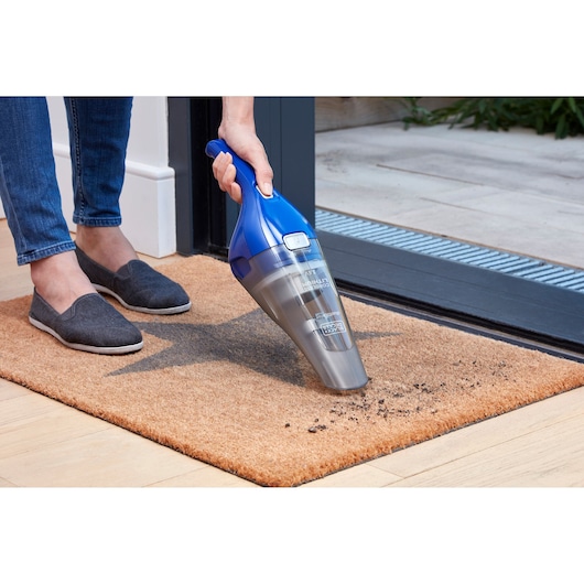 BLACK+DECKER NVC115WA handheld vacuum cleaning dirt from a doormat near a door, SKU NVC115WA.