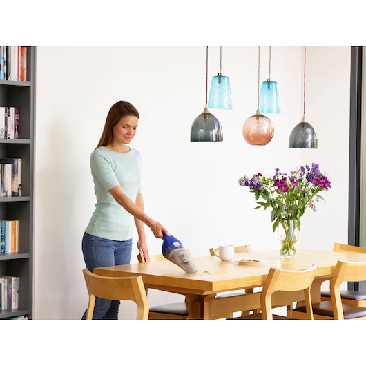BLACKDECKER NVC115WA handheld vacuum cleaning crumbs on dining table in modern kitchen setting.