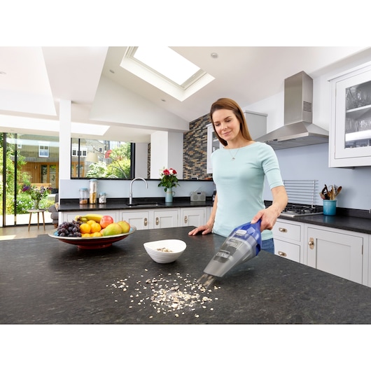 BLACK+DECKER NVC115WA handheld vacuum cleaning oats on kitchen counter near fruit bowl, side view.