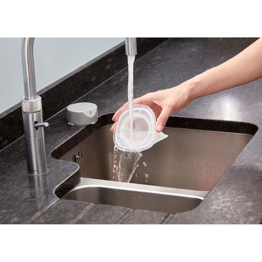 BLACKDECKER NVC115WA vacuum filter being rinsed under tap water in a kitchen sink, close-up angle.