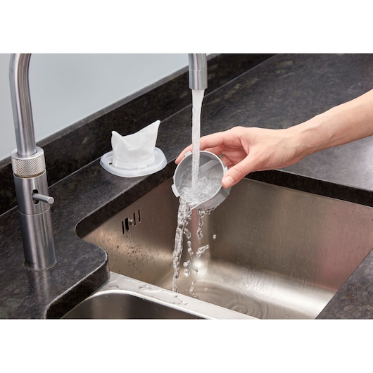 Photo of BLACKDECKER NVC220WC vacuum filter being cleaned under running water in a kitchen sink.