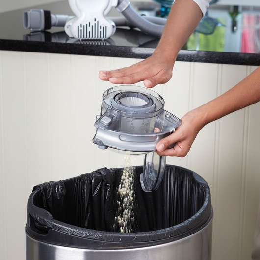 Photo of BLACKDECKER PD1020L vacuum dustbin being emptied into a trash can by hand, indoor setting.