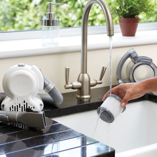 BLACKDECKER PD1020L handheld vacuum filter being rinsed under kitchen faucet, vacuum parts on counter.