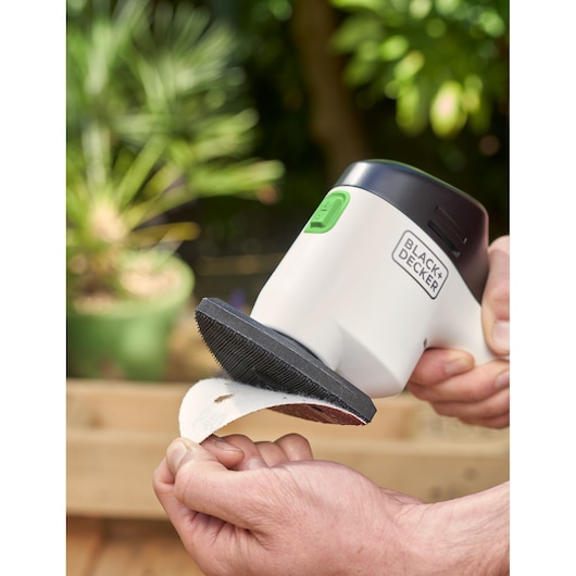 BLACK+DECKER REVDS12C detail sander held in hand, attaching sandpaper, outdoor background.