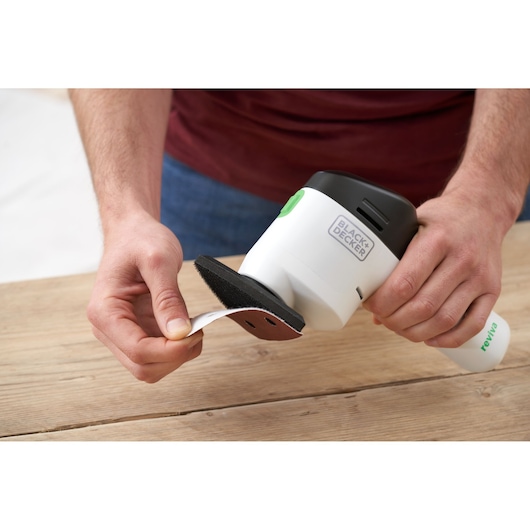 Photo of BLACK+DECKER REVDS12C detail sander held by hands, applying a sandpaper sheet to the sanding base.
