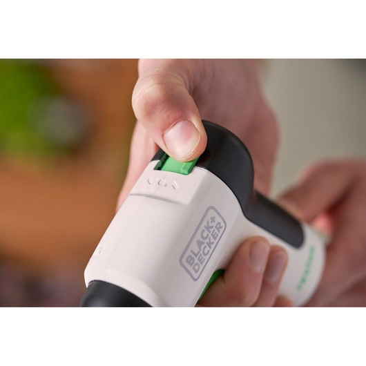 Close-up photo of hand operating BLACK+DECKER REVSD4C screwdriver, showing green switch and logo.