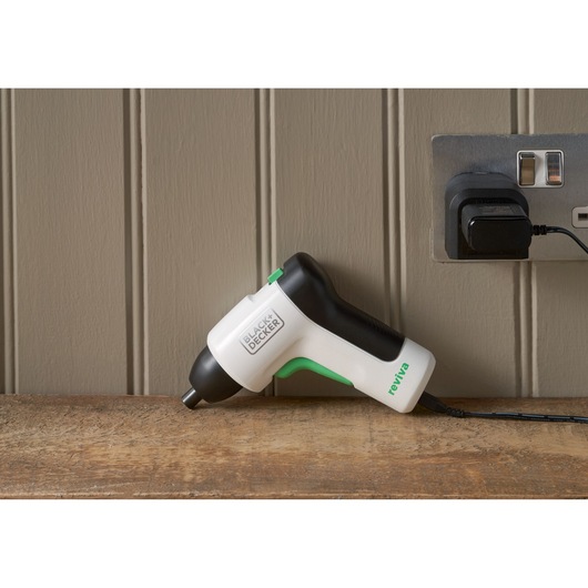 BLACK+DECKER REVSD4C cordless screwdriver white and black with green accents charging on wooden surface.