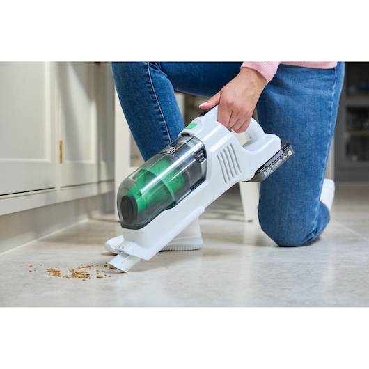 BLACK+DECKER REVSV18D1 handheld vacuum cleaner with green accents being used to clean crumbs on kitchen floor.