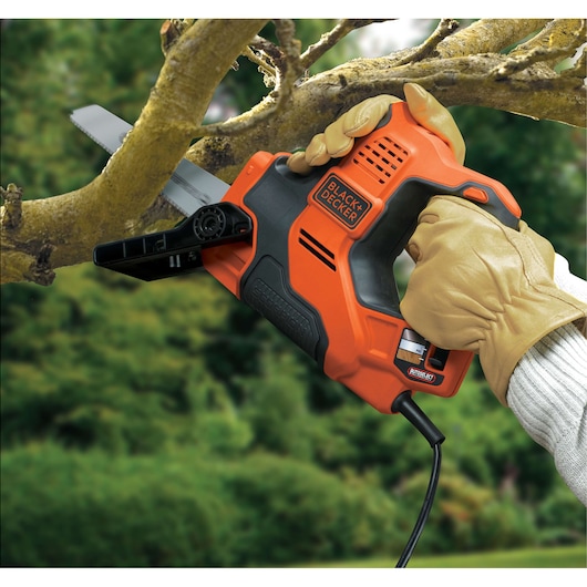Photo of BLACK+DECKER RS890K orange and black electric saw cutting a tree branch outdoors, operated by gloved hands.