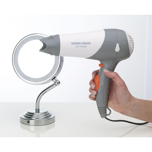 Photo of BLACK+DECKER SC800 hair dryer in gray and white, held in hand, next to a chrome makeup mirror, side angle.