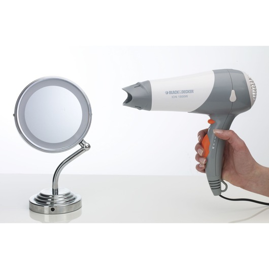 Photo of BLACK+DECKER SC800 grey and white hair dryer held in hand, next to a round chrome mirror, side angle.