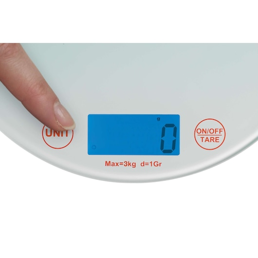 A close-up view of a digital kitchen scale with a blue backlit display showing '0'. A finger is pressing the 'UNIT' button on the left side. The scale also has an 'ON/OFF TARE' button on the right and red text below the display indicating Max=3kg, d=1Gr.