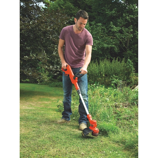 Photo of person using BLACKDECKER ST4525 orange and black grass trimmer in a garden.
