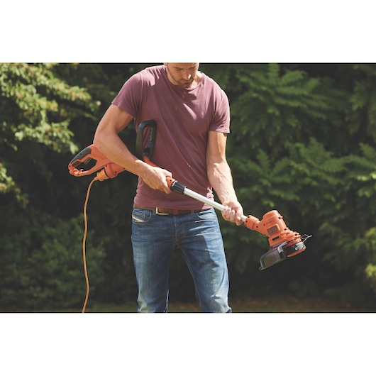 Photo of a person using a BLACKDECKER ST4525 orange electric grass trimmer outdoors.