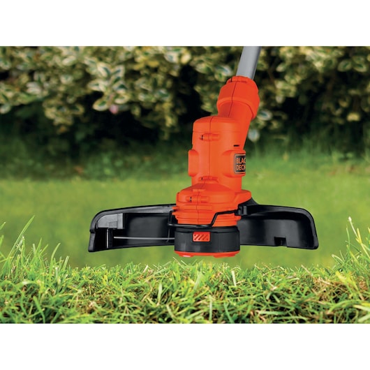 Photo of BLACK+DECKER ST4525 grass trimmer cutting green grass outdoors, close-up side view of orange and black tool.