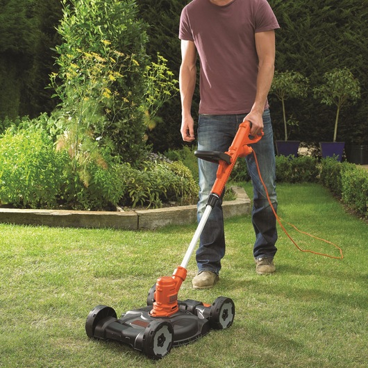 Photo of BLACKDECKER ST5530CMCAK lawn mower with orange handle used on grass in a garden setting.