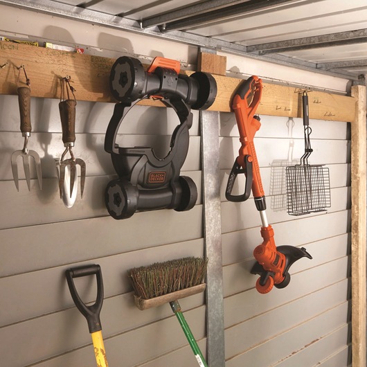 Photo of BLACKDECKER ST5530CMCAK orange and black garden tool stored hanging on a wooden rack in a shed.